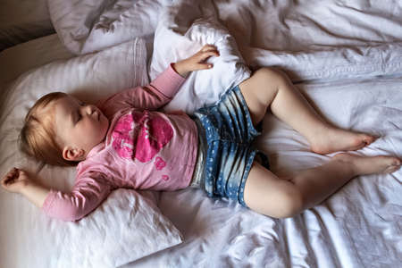 Sleepy little girl child lies in bed and cries. Morning time.の写真素材