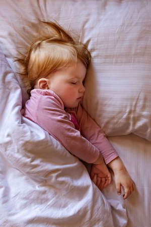 Sleepy little girl child lies in bed and cries. Morning time.の写真素材