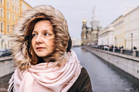 A young woman stands on the embankment of the river in winter. Middle-aged woman in a hood and a scarf, a winter green jacketの写真素材
