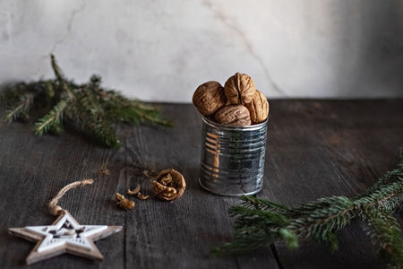 Walnuts in a tin Cup with spruce twigs and a wooden star on a wooden table. Christmas card. Low key.