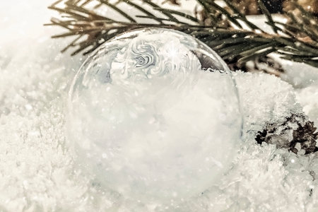 Frozen bubble with ice crystals on snow with fir branch at sunset. Christmas background.の写真素材