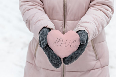 Women's hands in warm gray mittens with a snowy pink heart. The Concept Of Valentine's Day. The inscription on the heart Love.の写真素材