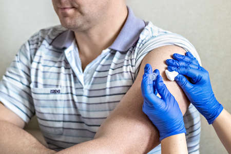 A doctor vaccinates a man against coronavirus at a clinic. Close-up. The concept of vaccination,...