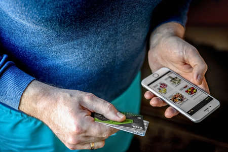 The man is holding a smartphone and bank cards. Pay for purchases online.のeditorial素材