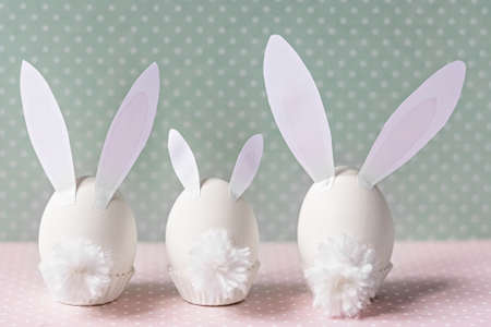 White chicken eggs with bunny ears and tails on bed flowers background. A family. Happy Easter holiday concept.の写真素材