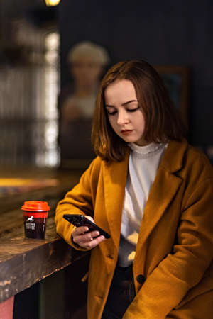 Young girl in a cafe, with a cup of coffee looking at the phone.のeditorial素材