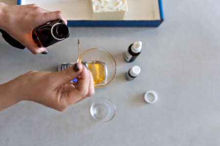 A soap-maker woman weighs aromatic oils for making cosmetics on a kitchen scale. Home spa. Small business.の写真素材