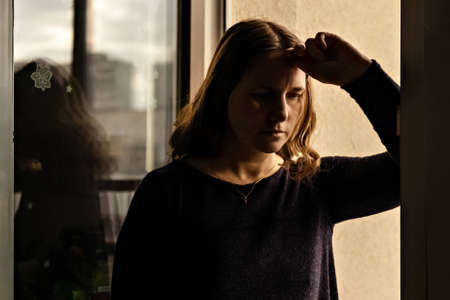 Portrait of a young woman at the window at sunset.の写真素材