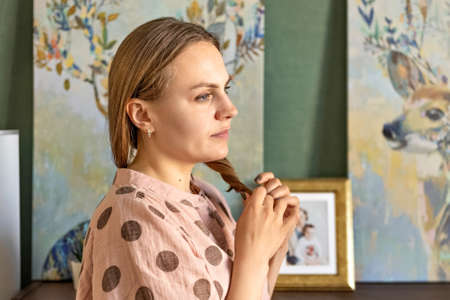 Portrait of a young woman straightening her hair in a room at home. Home environment. Interior.