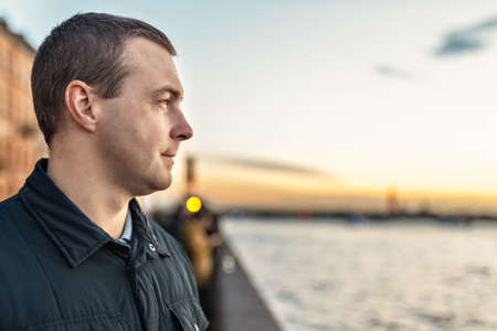 Portrait of a young man watching the sunset on the embankment of the river in the city.の写真素材