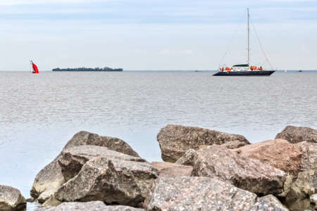 Granite stones in the water on the shore of the Gulf of Finland. Sailboats float on the water.の写真素材