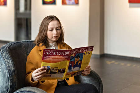 A young woman sits in a chair in the great hall of the art gallery looking through a booklet.のeditorial素材
