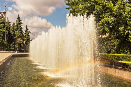 A working fountain in the park with a rainbow from splashes.の写真素材
