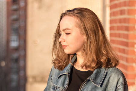 Portrait of a young teenage girl against a brick wall at sunset.
