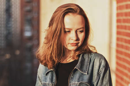Portrait of a young teenage girl against a brick wall at sunset.の写真素材