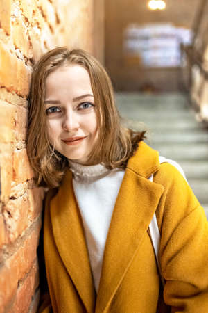 Portrait of a young woman in a bright yellow coat against the background of a brick wall by the window.In the sunshineの写真素材