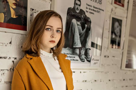 Portrait of a young teenage girl against a white brick wall with a poster.のeditorial素材