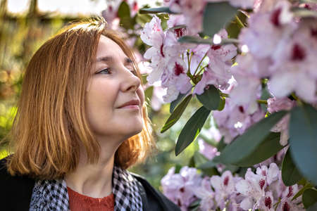Portrait of a young happy woman with red hair. A blooming spring garden. Pink Rhododendron Flowers.の写真素材