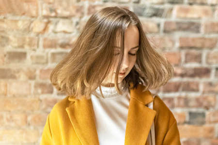 Portrait of a young woman in a bright yellow coat against the background of a brick wall by the window.In the sunshineの写真素材