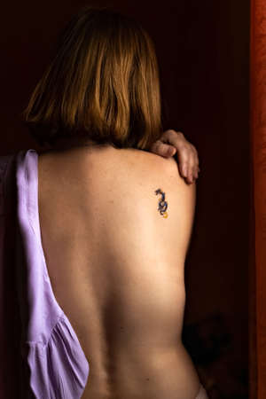 The naked back of a young woman with red hair and a tattoo on her shoulder.の写真素材