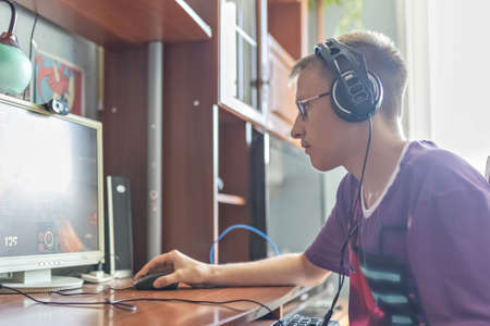 A teenage boy, a young man playing video games on a computer, using technology, wearing headphones, using a computer. He plays video games. Using headphonesの写真素材