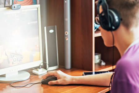 A teenage boy, a young man playing video games on a computer, using technology, wearing headphones, using a computer. He plays video games. Using headphonesの写真素材