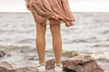 A young woman stands on the rocky shore of the sea. A dress flying in the wind close-up.の写真素材