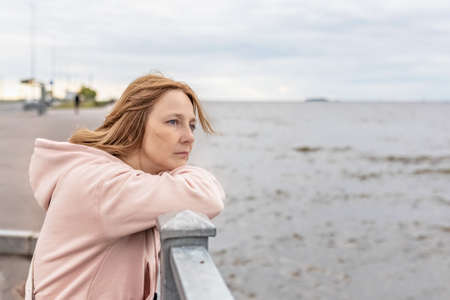 A young woman on a cloudy evening stands on the embankment and looks at the sea.の写真素材