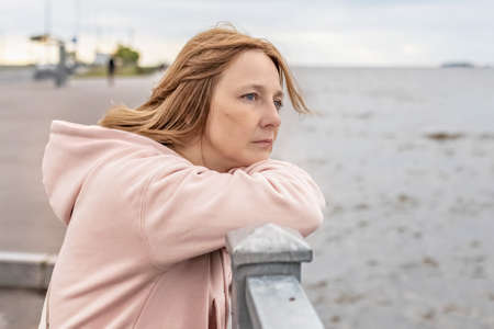 A young woman on a cloudy evening stands on the embankment and looks at the sea.