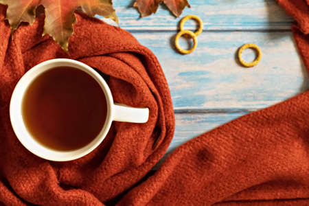 Autumn composition, a cup of hot tea, a warm terracotta scarf, fallen leaves and drying on the background of a blue wooden table. Flat lay.の写真素材