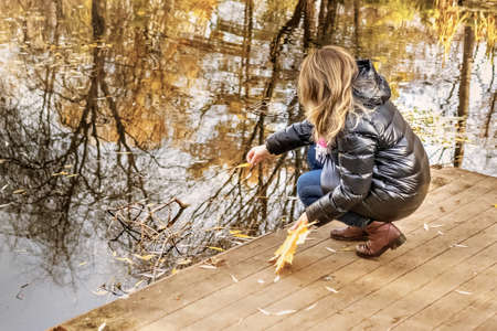 A young woman on the shore of a pond in an autumn park.の写真素材