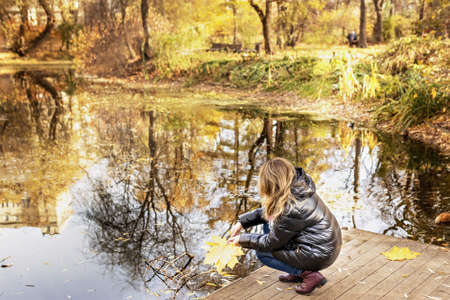 A young woman on the shore of a pond in an autumn park.の写真素材