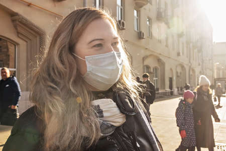 Portrait of a young woman in a protective medical mask on her face on a city street. Pandemic...