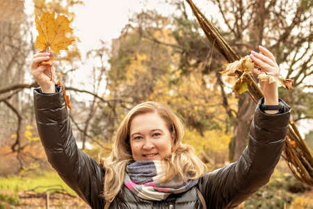 Portrait of a young woman near a seasonal outdoor installation in an autumn park. Fallen yellow leaves in the hands, flying.の写真素材