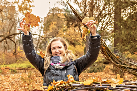 Portrait of a young woman near a seasonal outdoor installation in an autumn park. Fallen yellow leaves in the hands, flying.の写真素材