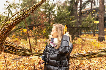 Portrait of a young woman near a seasonal outdoor installation in an autumn park. Fallen yellow leaves in the hands, flying.の写真素材