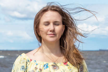 A large portrait of a young woman with fluttering hair in the wind on the seashore.