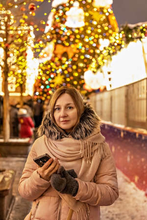 A young woman on the street, in the square with a Christmas tree and Christmas decorations.Celebrating New Year and Christmasの写真素材