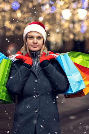 A young woman's Christmas shopping. Colorful bright paper bags with gifts. A walk through the Christmas shops of a young beautiful woman. Garlands, lights.Celebrating the New Year.の写真素材