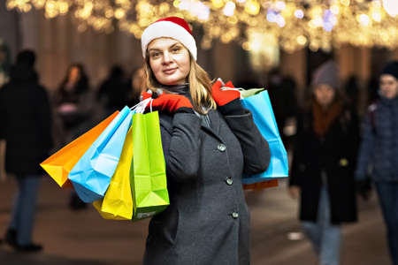 A young woman's Christmas shopping. Colorful bright paper bags with gifts. A walk through the Christmas shops of a young beautiful woman. Garlands, lights.Celebrating the New Year.の写真素材