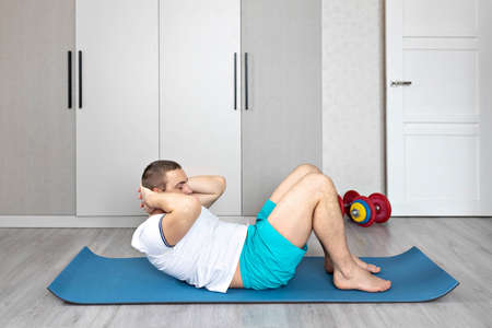 A strong, healthy man with muscles, training at home. Exercises for the muscles of the press.の写真素材