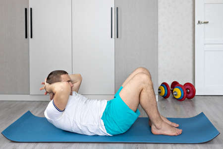 A strong, healthy man with muscles, training at home. Exercises for the muscles of the press.の写真素材