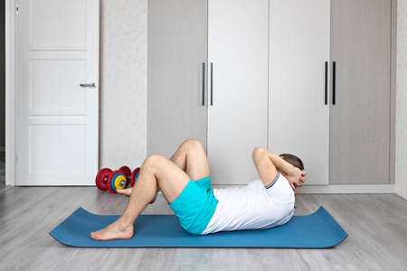 A strong, healthy man with muscles, training at home. Exercises for the muscles of the press.の写真素材