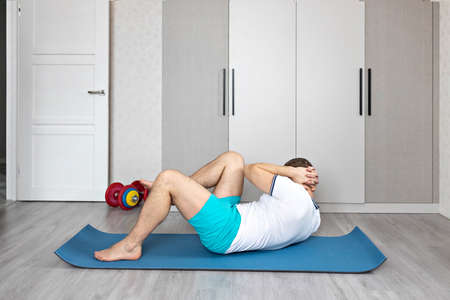 A strong, healthy man with muscles, training at home. Exercises for the muscles of the press.の写真素材