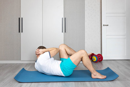 A strong, healthy man with muscles, training at home. Exercises for the muscles of the press.の写真素材