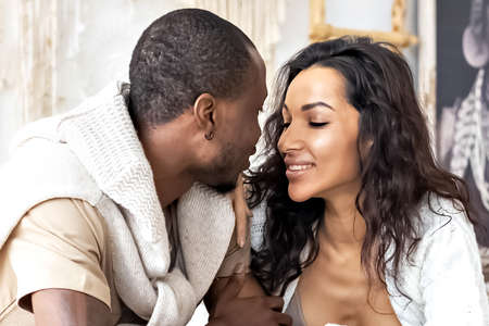 A couple in love - a black man and a mulatto woman on a bed in a bright room. Diverse family.の写真素材