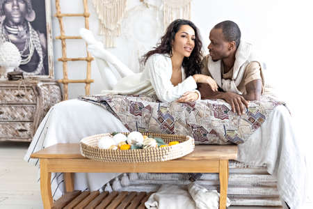 A couple in love - a black man and a mulatto woman on a bed in a bright room. Diverse family.の写真素材