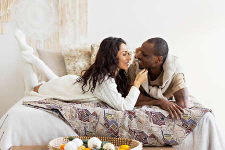 A couple in love - a black man and a mulatto woman on a bed in a bright room. Diverse family.の写真素材