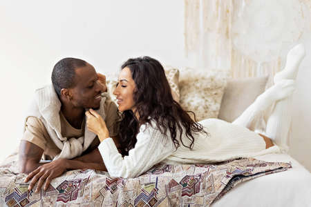 A couple in love - a black man and a mulatto woman on a bed in a bright room. Diverse family.の写真素材