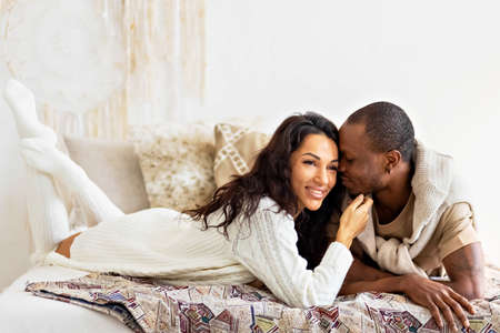A couple in love - a black man and a mulatto woman on a bed in a bright room. Diverse family.の写真素材